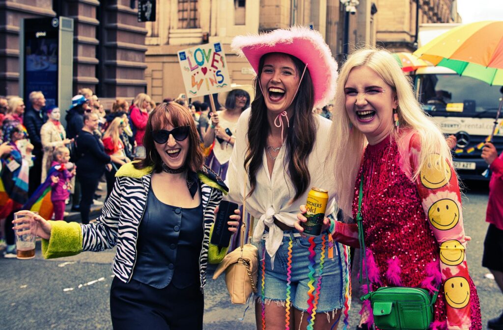 Happy participants celebrating at Manchester Pride Parade, showcasing colorful attire and joyful expressions.