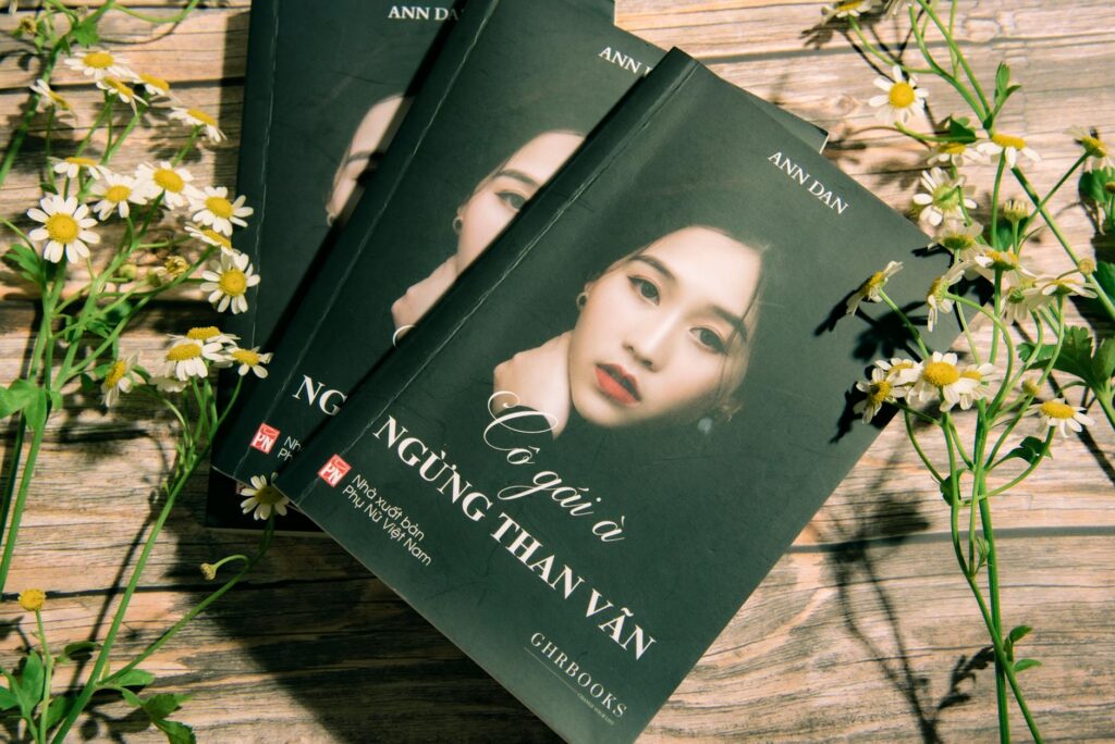 Vietnamese book on wooden surface surrounded by chamomile flowers.