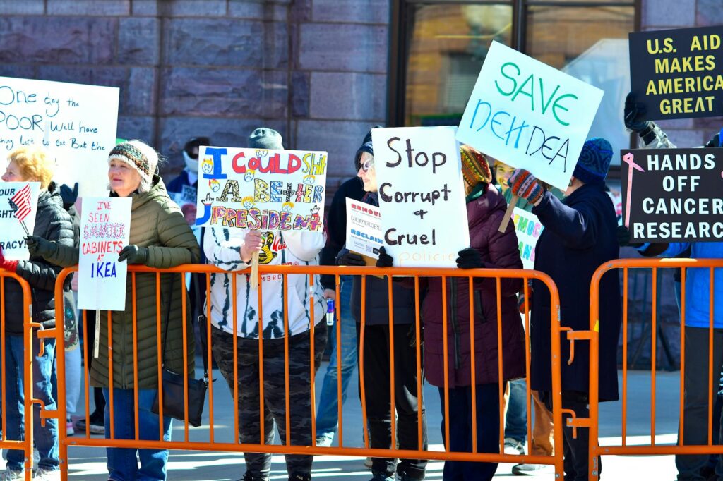 A group of people holding signs in a street protest, expressing dissent against political policies.
