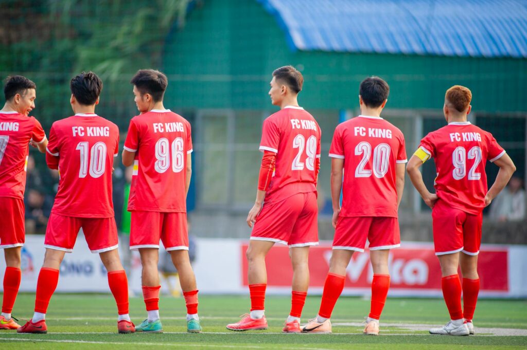 Football players in red uniforms from FC King standing on a field in Hà Nội, Vietnam.