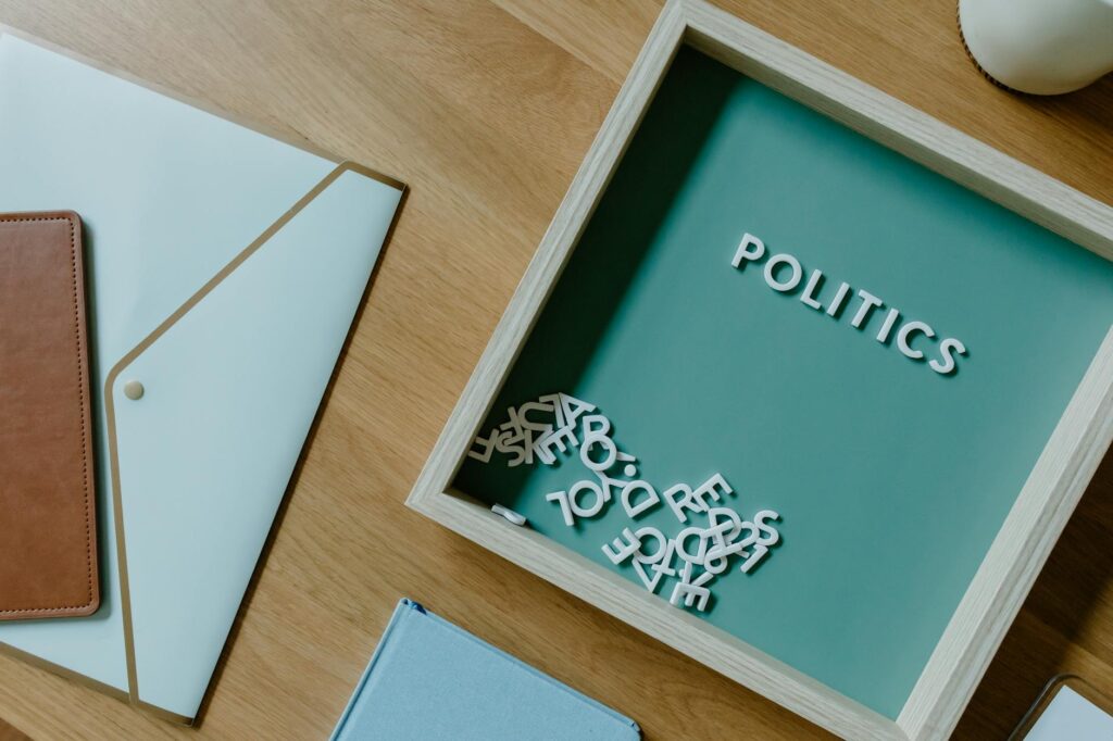 Top view of a box with 'POLITICS' text alongside office items on a wooden desk.