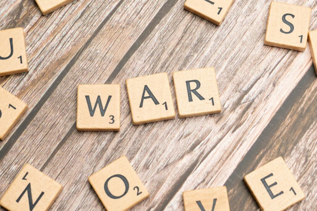 Close-up of wooden scrabble tiles spelling 'WAR' on a wooden background.