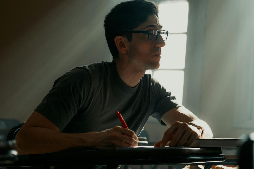 A young adult writing attentively in a classroom illuminated by soft sunlight.