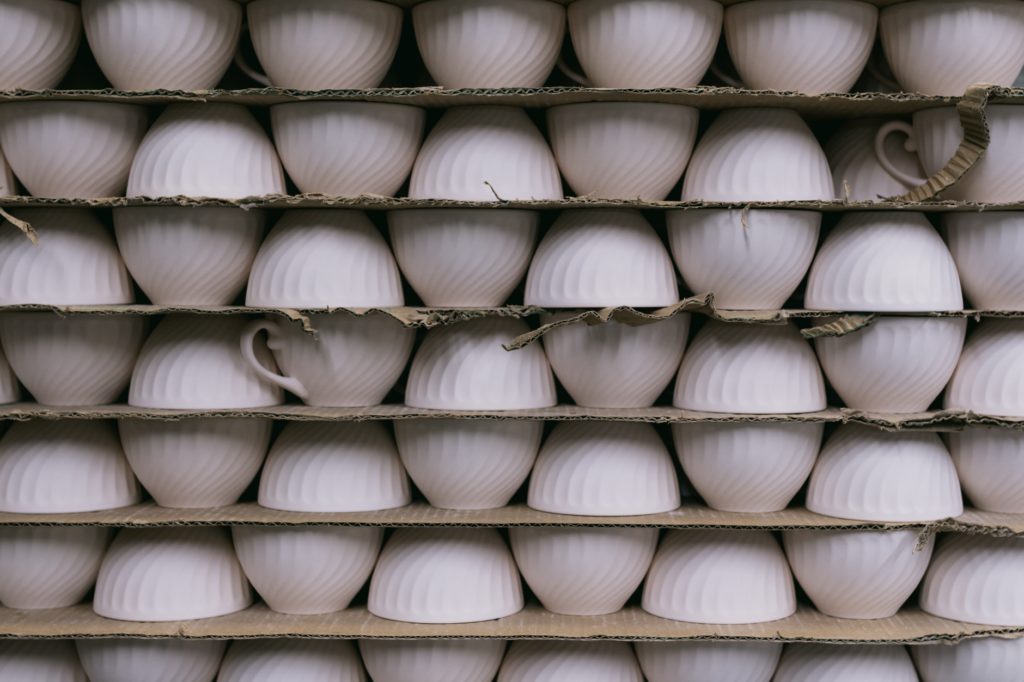 Multiple ceramic cups stacked in rows on shelves, ready for packaging or sale.