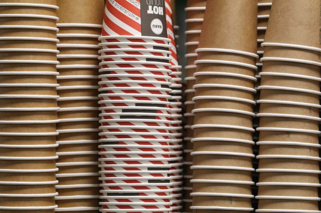 Close-up of paper coffee cups with red striped design and plain brown cups stacked together.