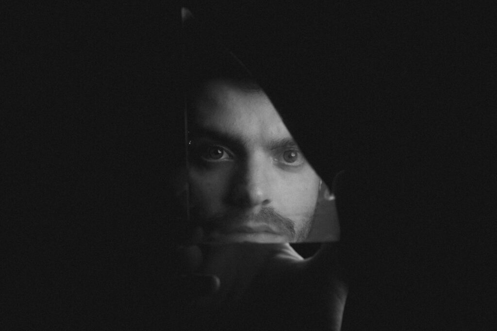 A dramatic black and white portrait of a man reflected in a broken mirror fragment.