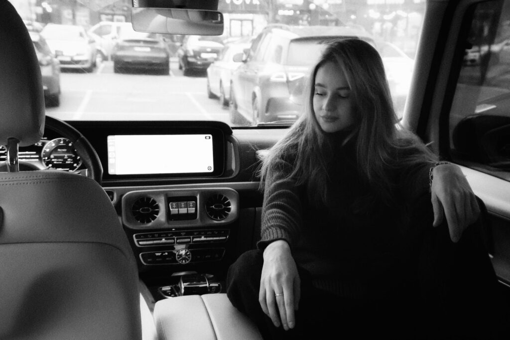 Black and white photo of a woman relaxing inside a luxury car, creating a serene ambiance.