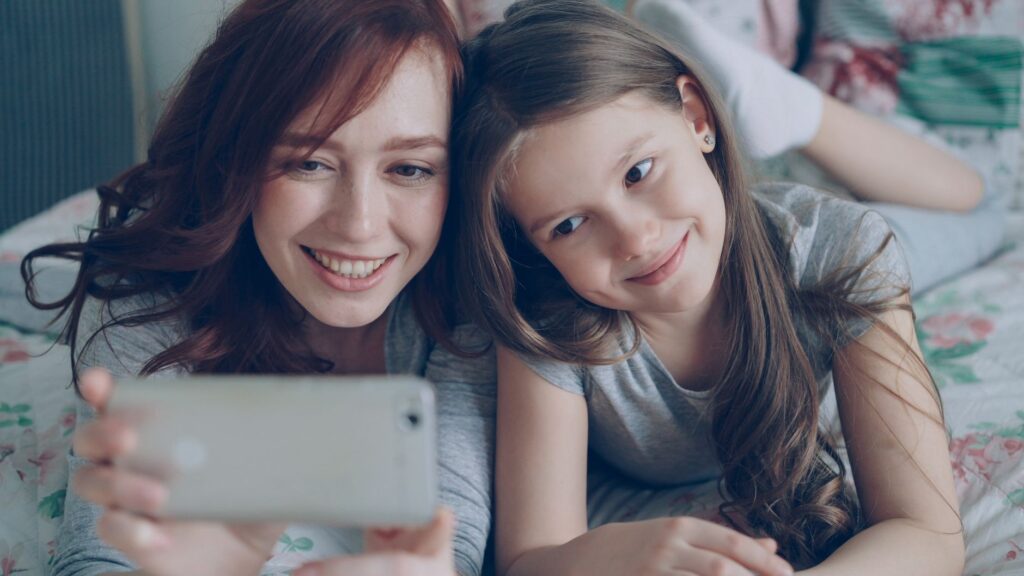 A joyful mother and daughter taking a selfie together on the bed.