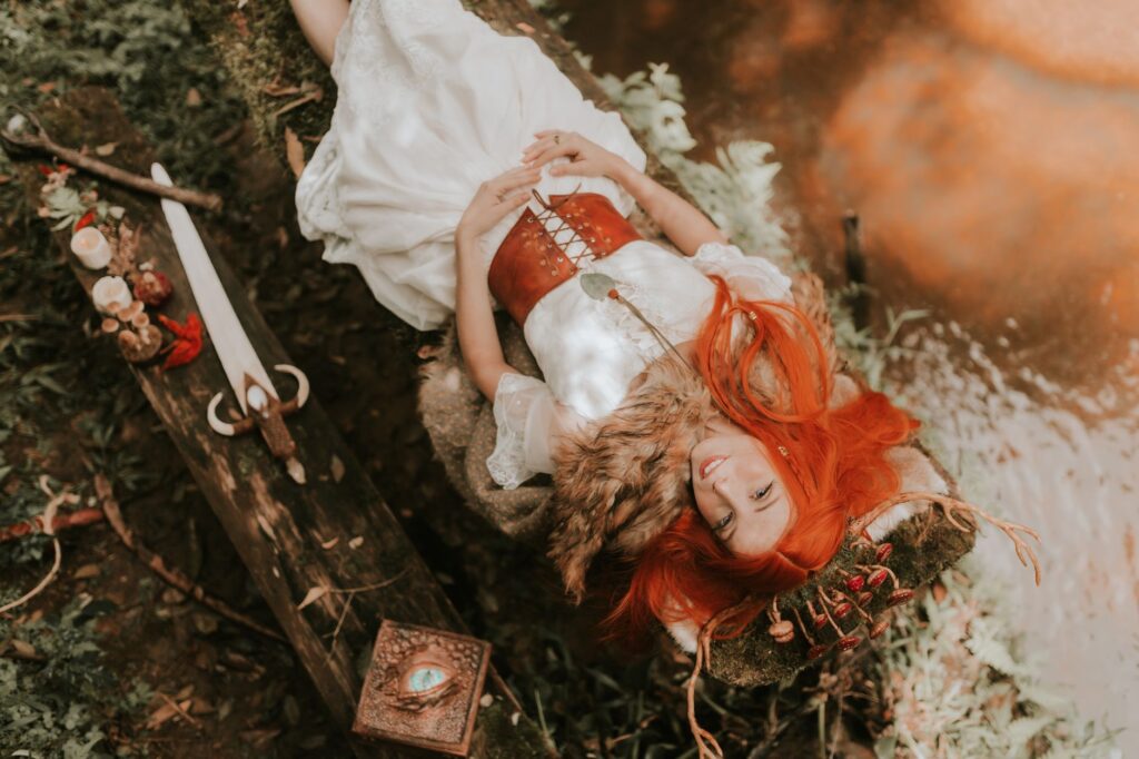 A woman in fantasy cosplay attire lies by a river, creating a mystical scene.